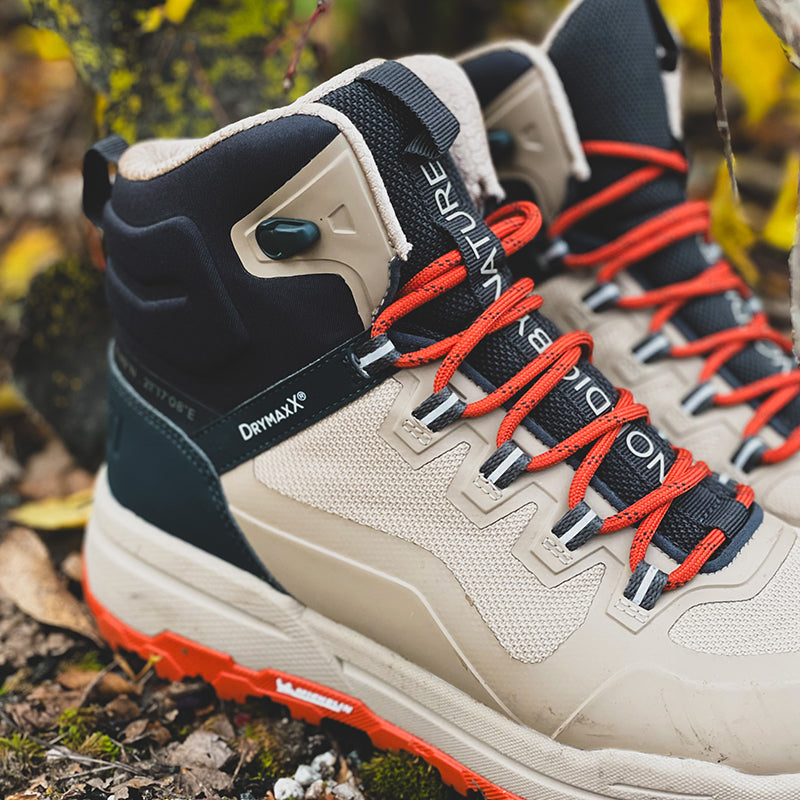 Nahaufnahme der Halti Hiker Kuru DrymaxX Damenschuhe in Beige/Schwarz mit roten Schnürsenkeln, wasserdicht, auf felsigem, belaubtem Boden.