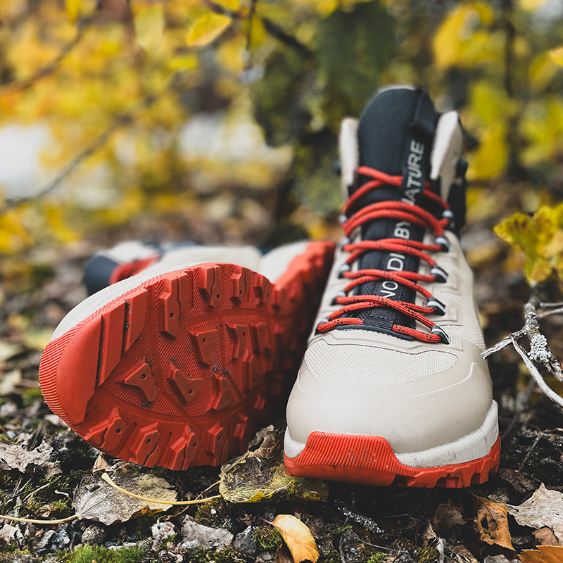 Ein Paar Halti Hiker Kuru DrymaxX Outdoor-Schuhe für Damen in Beige/Rot liegt inmitten von Blättern – eines aufrecht, eines auf der Seite liegend.