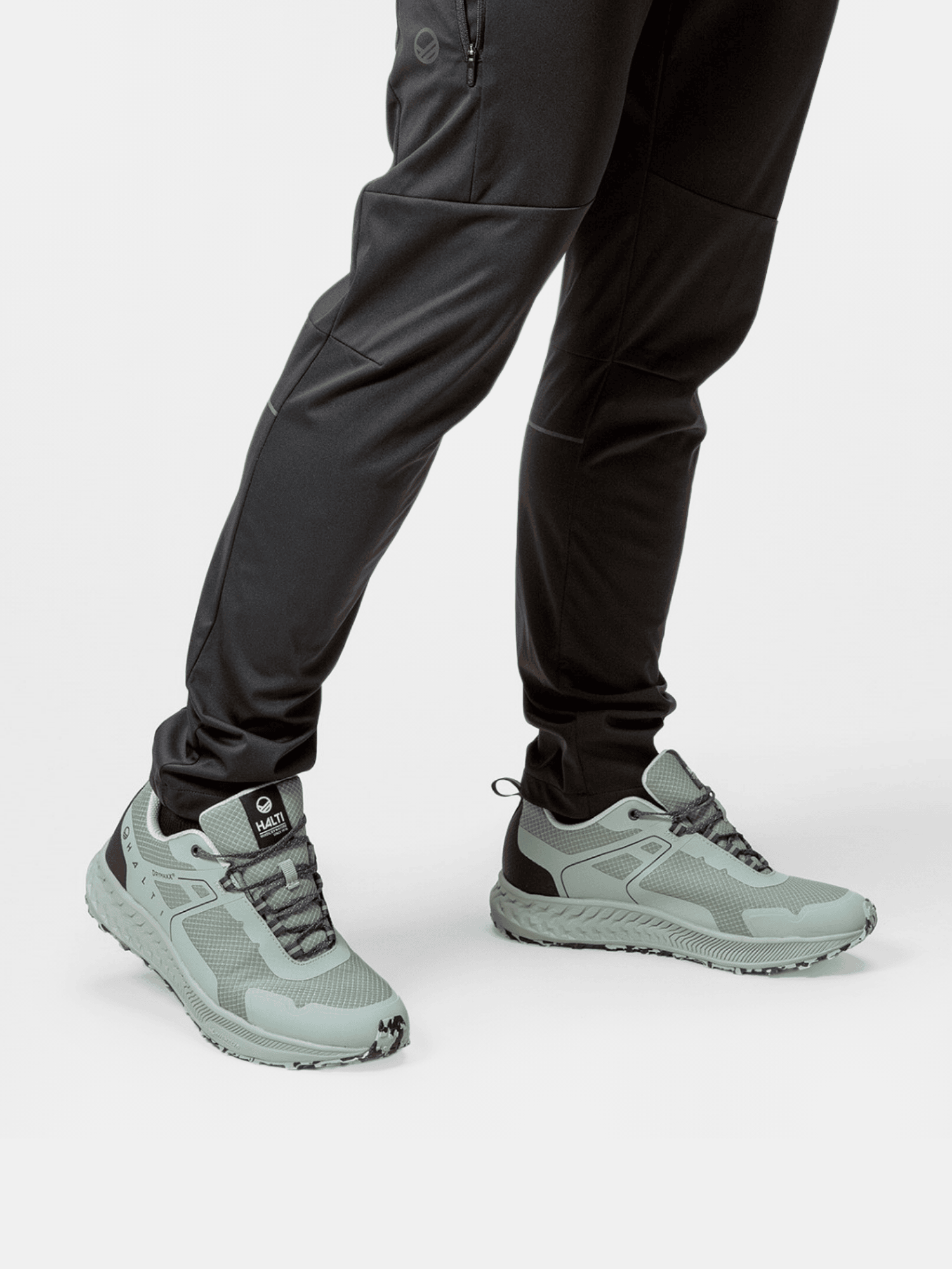 Mann trägt Halti Pallas Low 2 DrymaxX Hybrid Sneaker Herren in Hellgrau/Schwarz mit schwarzer Hose, auf weißem Hintergrund.