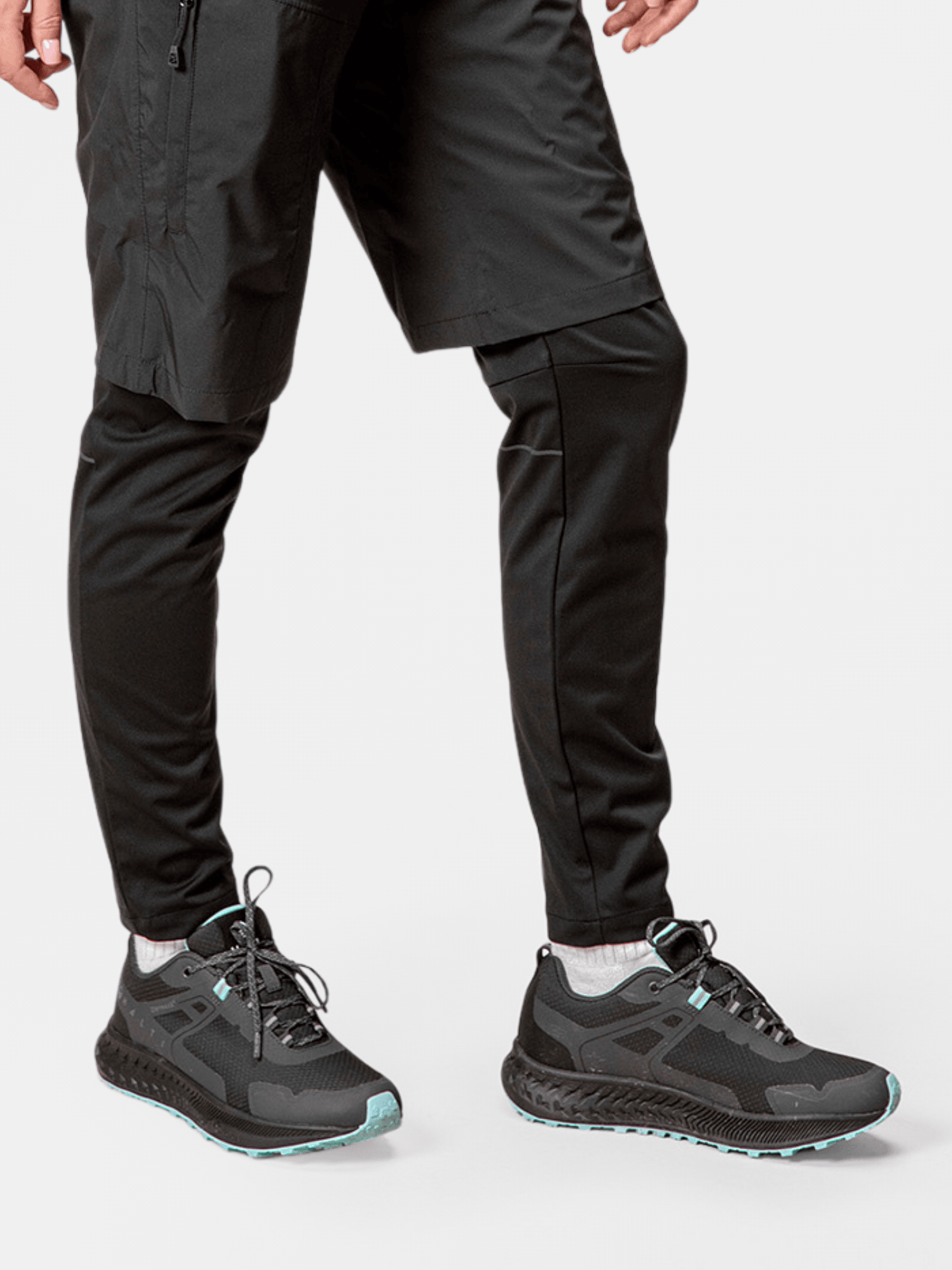 Person trägt Halti Pallas Low 2 DrymaxX Hybrid Sneaker Damen in Schwarz, mit schwarzen Hosen und Shorts, auf weißem Hintergrund.