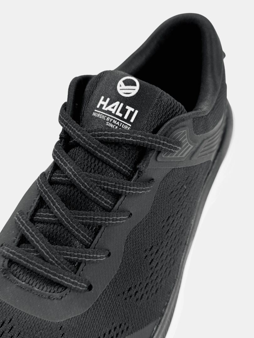 Nahaufnahme eines schwarzen Halti Tempo 3 Sneakers für Herren mit Schnürsenkeln, atmungsaktivem Mesh und weißer Sohle auf schlichtem Hintergrund.