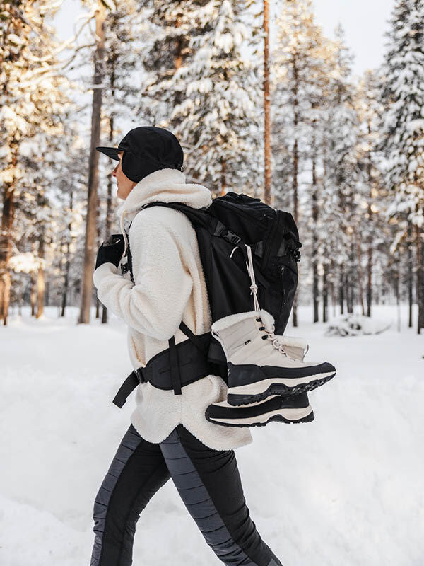 Person in Winterkleidung und Rucksack mit Halti Tornio 2 DX Winterschuhen bei einem Spaziergang in einem verschneiten Wald.