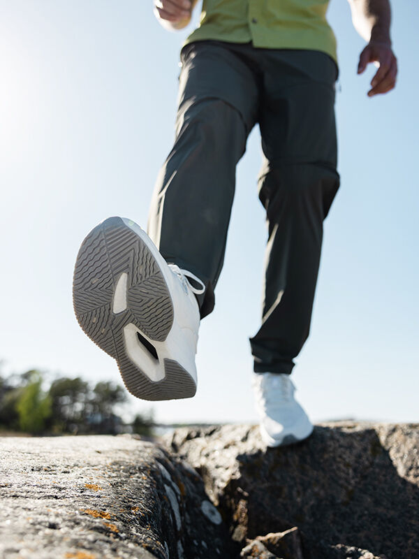 Eine Person schreitet über Felsen und präsentiert die Sohle ihrer weißen Halti Syke Sneaker Herren.