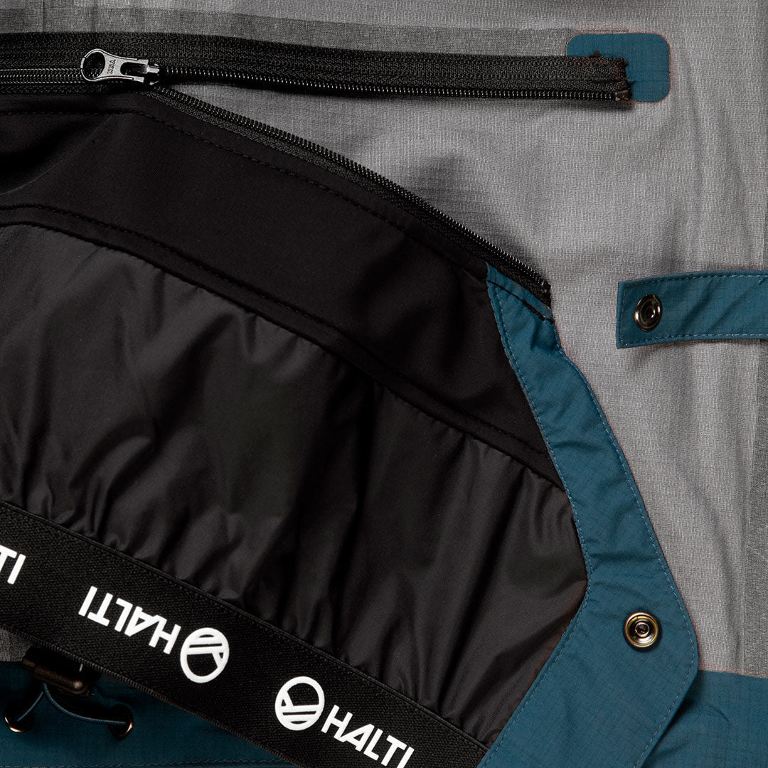 Nahaufnahme der Halti Alpine 3L DX Skijacke Unisex mit Reißverschlusstasche, Druckknopf und gebrandetem Gummiband.