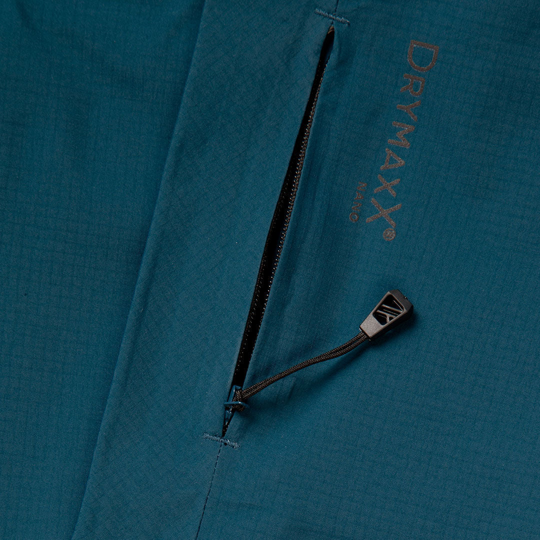 Eine Nahaufnahme einer tealfarbenen Halti Alpine 3L DX Skijacke Unisex mit einer Reißverschlusstasche und