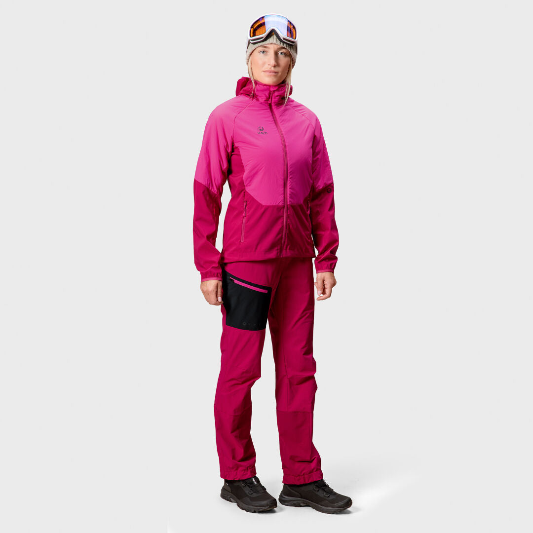 Person in leuchtend pinker Halti Crust Damen Layer Jacke, Hose aus X-Stretch-Material, schwarzen Schuhen und Skibrille auf der Stirn.