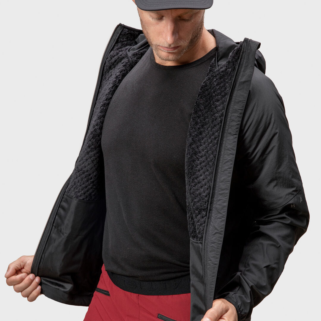 Ein Mann in einer schwarzen Halti Crust Herren Layer Jacke blickt nach unten und zeigt das Innenfutter aus X-Stretch-Material.