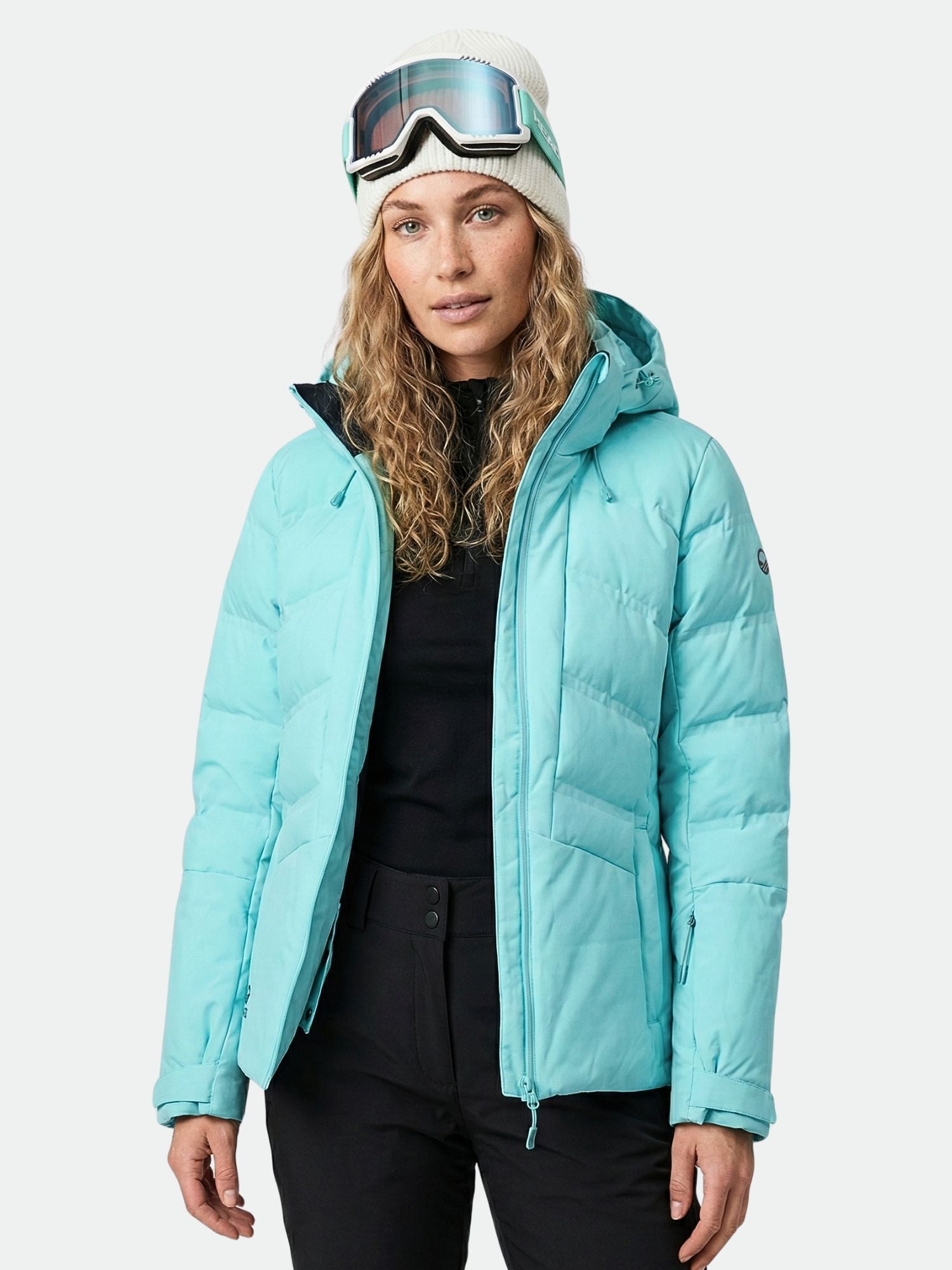 Frau in Halti Nordic Arcty Skijacke Damen und Skibrille, schwarze Hose, weiße Strickmütze, einfarbiger Hintergrund.