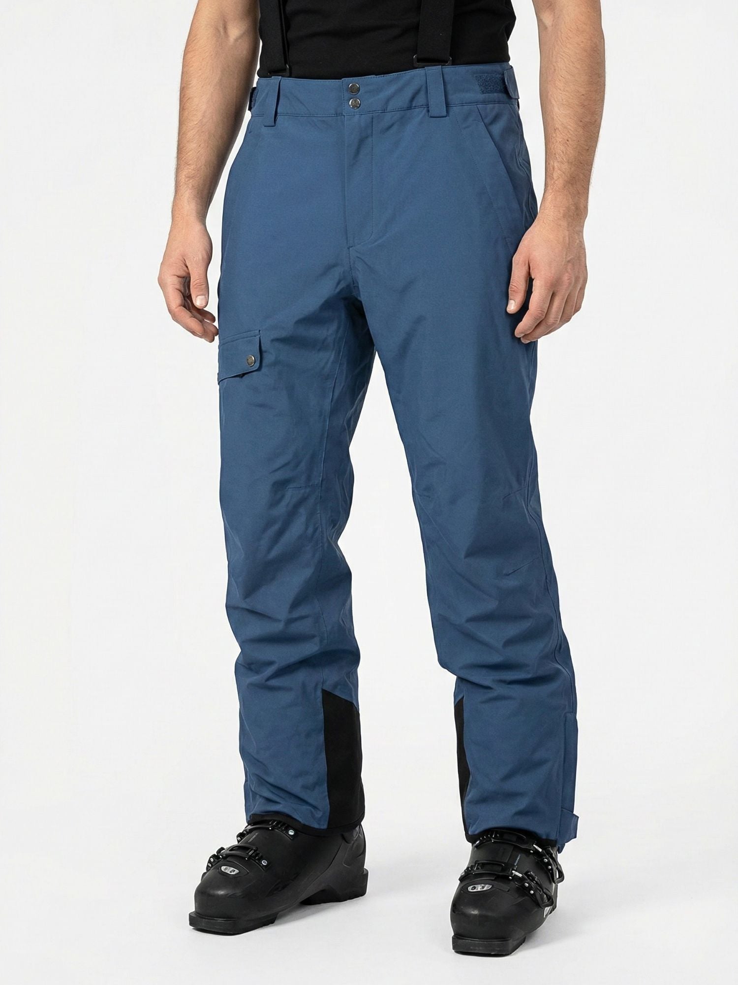 Eine Person in Halti Settler 3L DX Skihose Herren, schwarzen Skischuhen und einem schwarzen Hemd steht vor einem schlichten weißen Hintergrund.