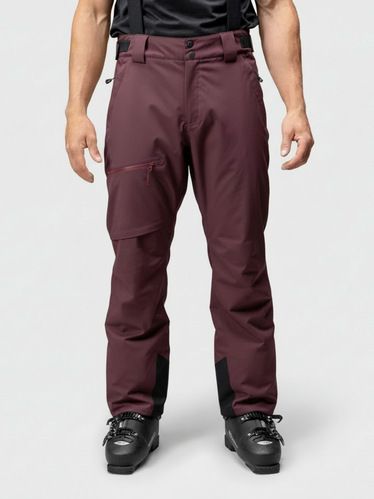 Eine Person trägt Halti Carvey DX Skihose Herren mit schwarzen Hosenträgern und Skistiefeln, stehend vor einem schlichten Hintergrund.