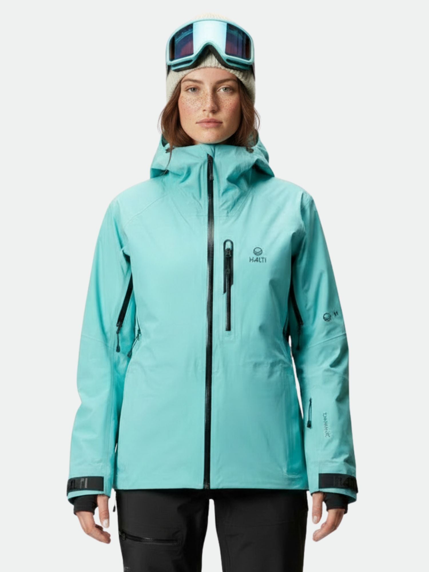 Eine Person mit einer Halti Alpine 3L DX Skijacke Damen, einer schwarzen Hose, einer Skibrille und einer grauen Mütze steht mit dem Gesicht nach vorne.