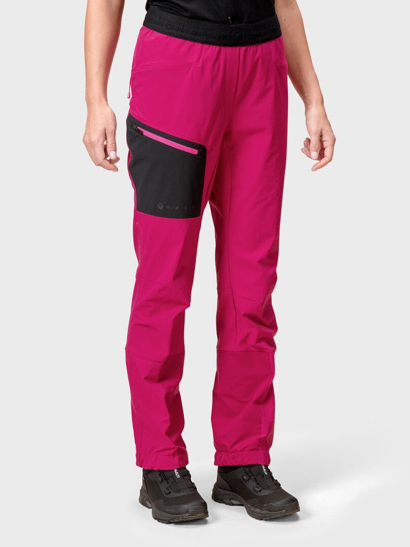 Eine Frau in Halti Adrenaline Lite Skitourenhose und schwarzen Schuhen steht vor einem schlichten hellen Hintergrund.