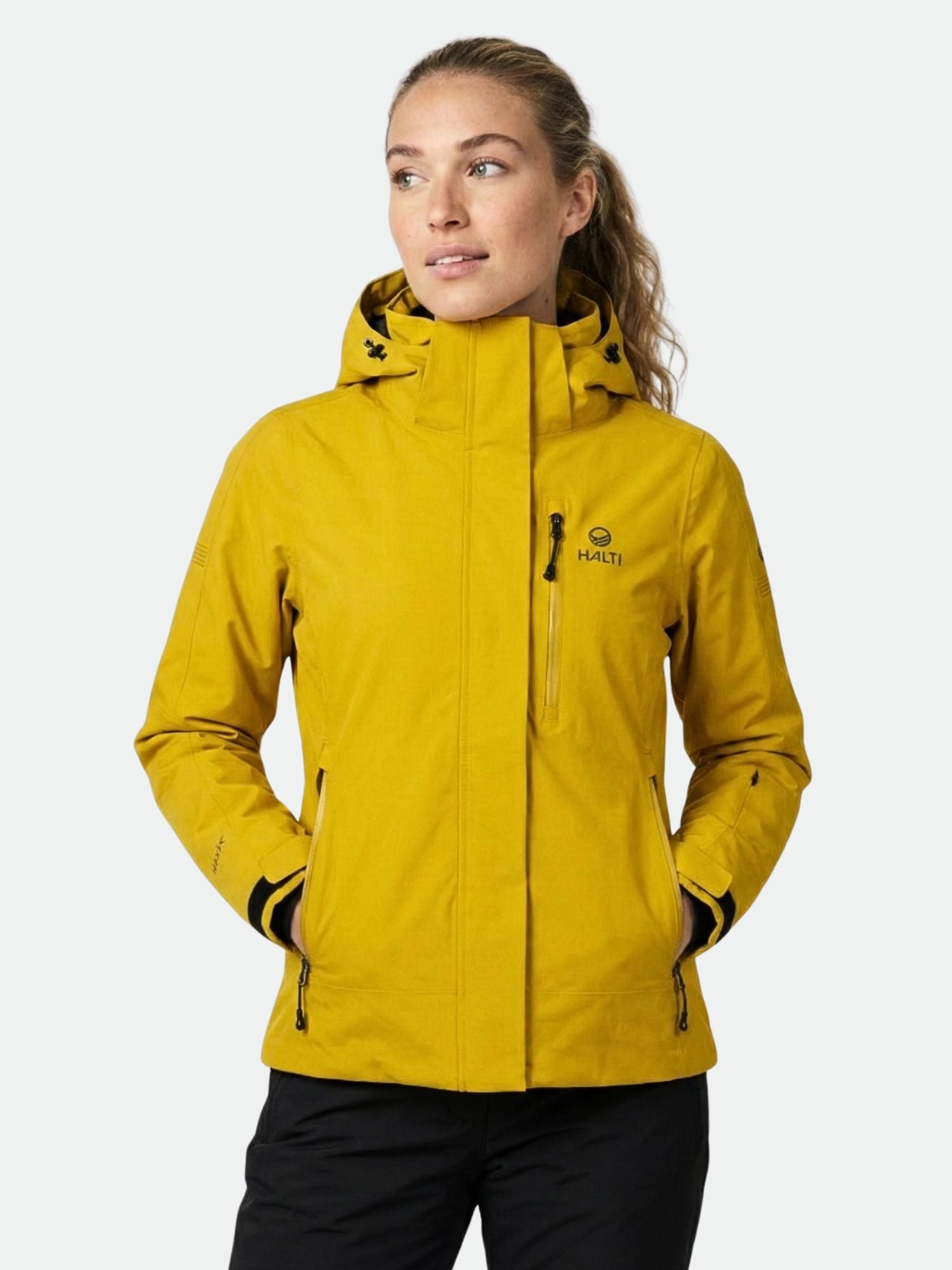 Eine Frau in einer gelben Halti Radius DX Skijacke Damen mit Taschen, ausgestattet mit wind- und wasserdichtem DrymaxX® Ultimate Tech.