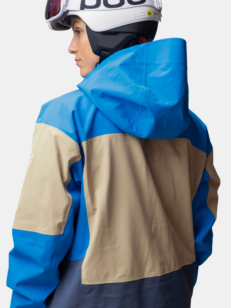Eine Person, die die Halti Rizle Unisex 3L DX Skijacke und einen weißen Helm trägt, wird von hinten gezeigt.