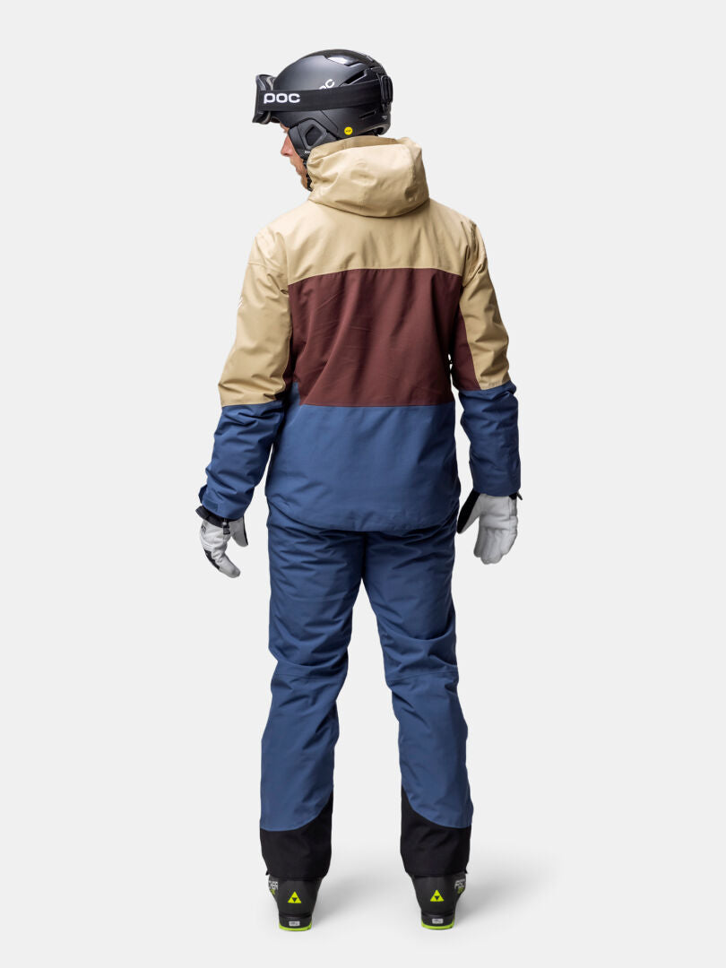 Person in Halti Melvik DX Skijacke Herren, Helm und Handschuhe an, von der Kamera abgewandt.