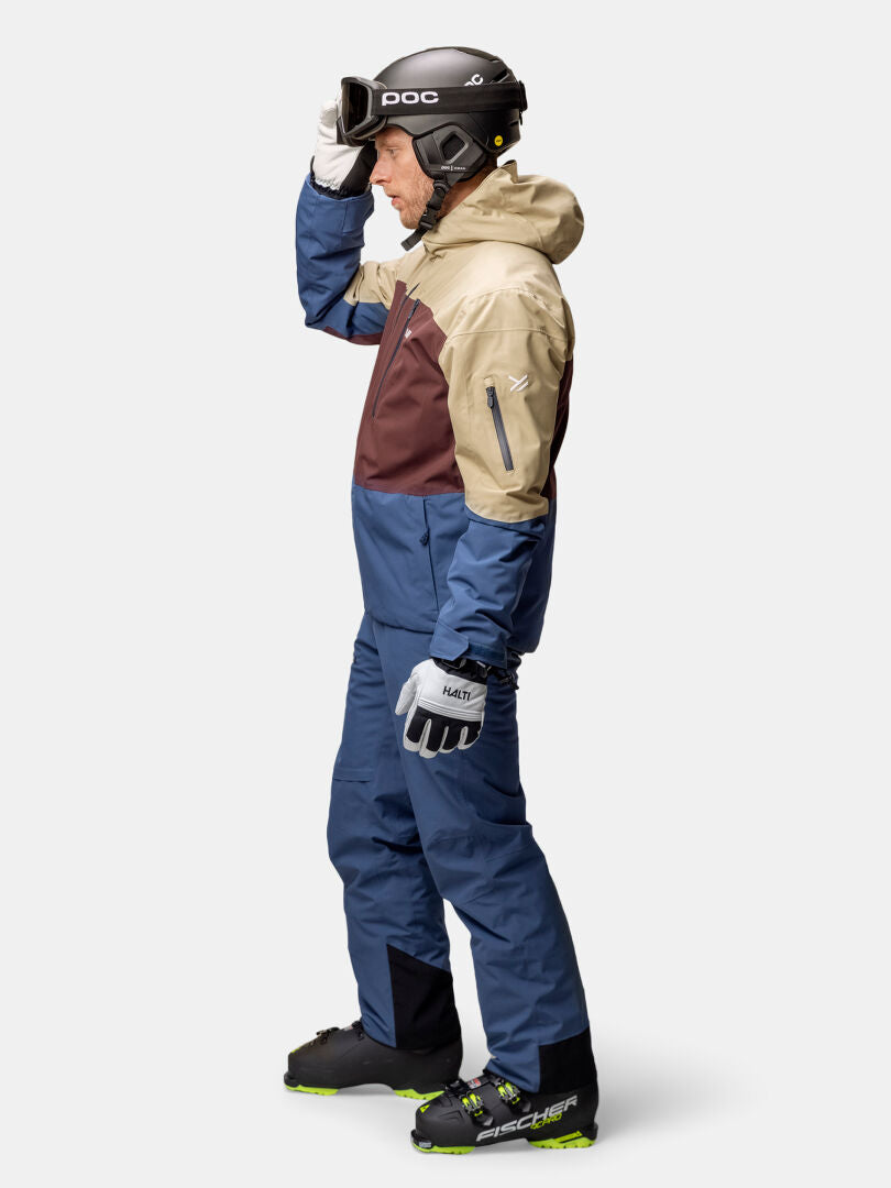 Mann in Halti Melvik DX Skijacke Herren, Helm und Brille steht im Profil und stellt seine Brille ein.
