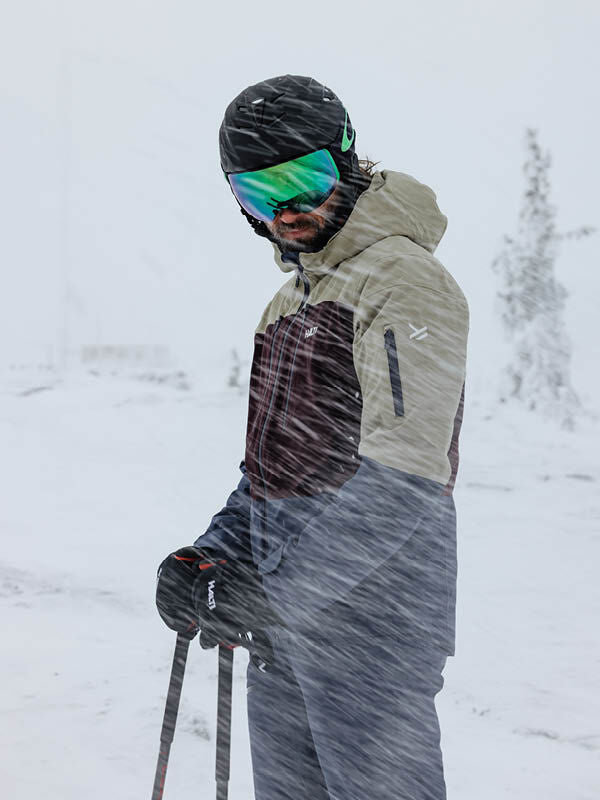 Ein Skifahrer in einer Halti Melvik DX Skijacke Herren steht mit Skistöcken im Schnee und bei Wind.