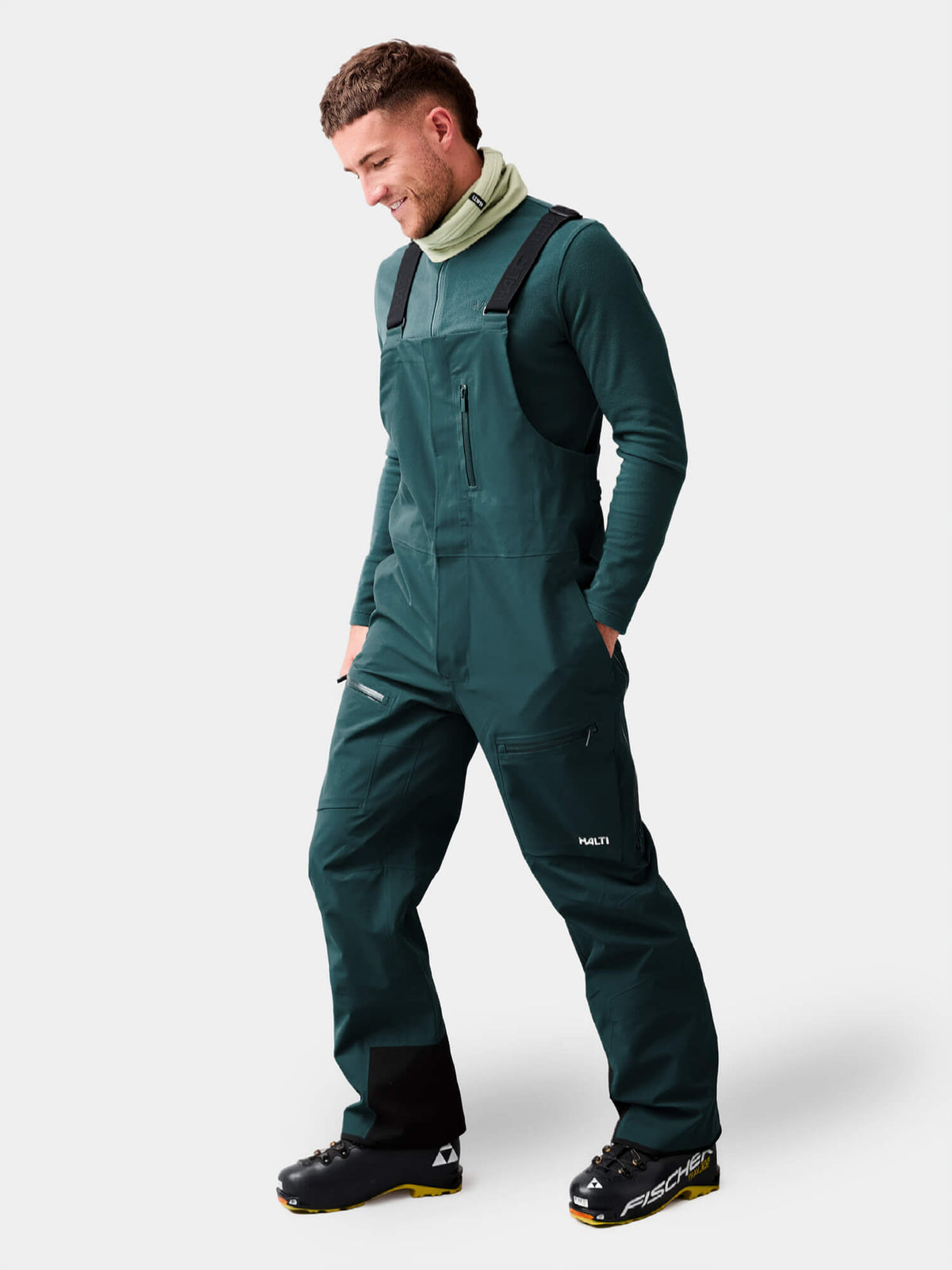 Eine Person, die dunkelgrüne Halti Rizle 3L DX Unisex-Skihosen mit Latz und Stiefel trägt.