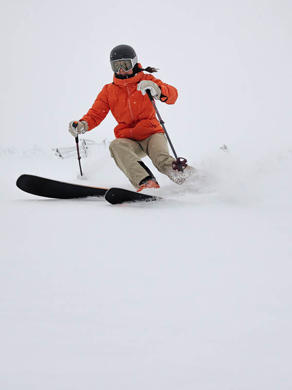 Mit der Halti Nordic Arcty II Skijacke Damen und Helm rast eine Skifahrerin bergab, während der Schnee von den Stöcken fliegt.