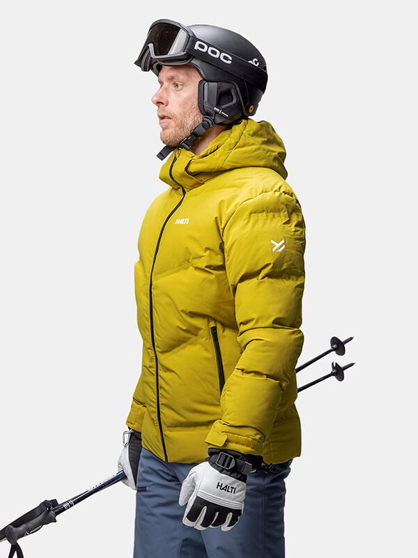 Mann in einer gelben Halti Nordic Arcty II Skijacke Herren, Helm, Brille und Skistöcken.