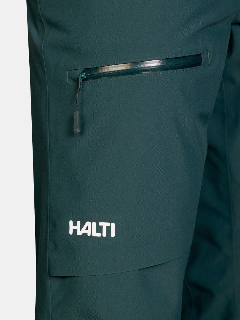 Nahaufnahme der dunkelgrünen, wasserdichten Hose Carvey II DX Skihose Damen mit einer Reißverschlusstasche und einem Logo am Saum.