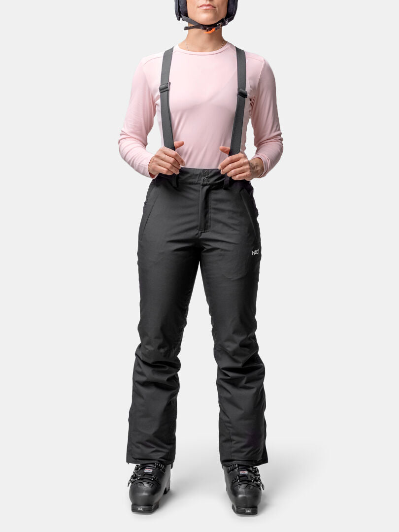 Person mit rosa Langarmshirt, Halti Glades II DX Skihose Damen, Skistiefel und Helm auf weißem Hintergrund.