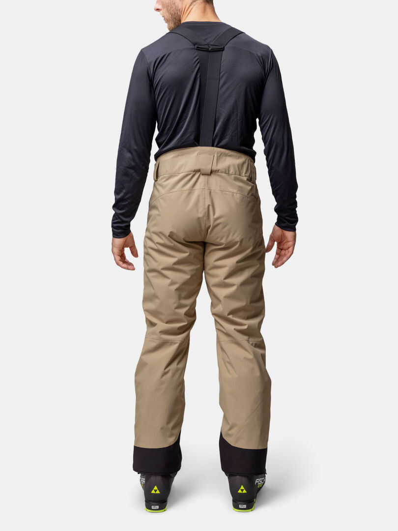 Eine Person in Halti Carvey II DX Skihose Herren mit Hosenträgern, schwarzem Hemd und Skischuhen, von hinten gesehen.