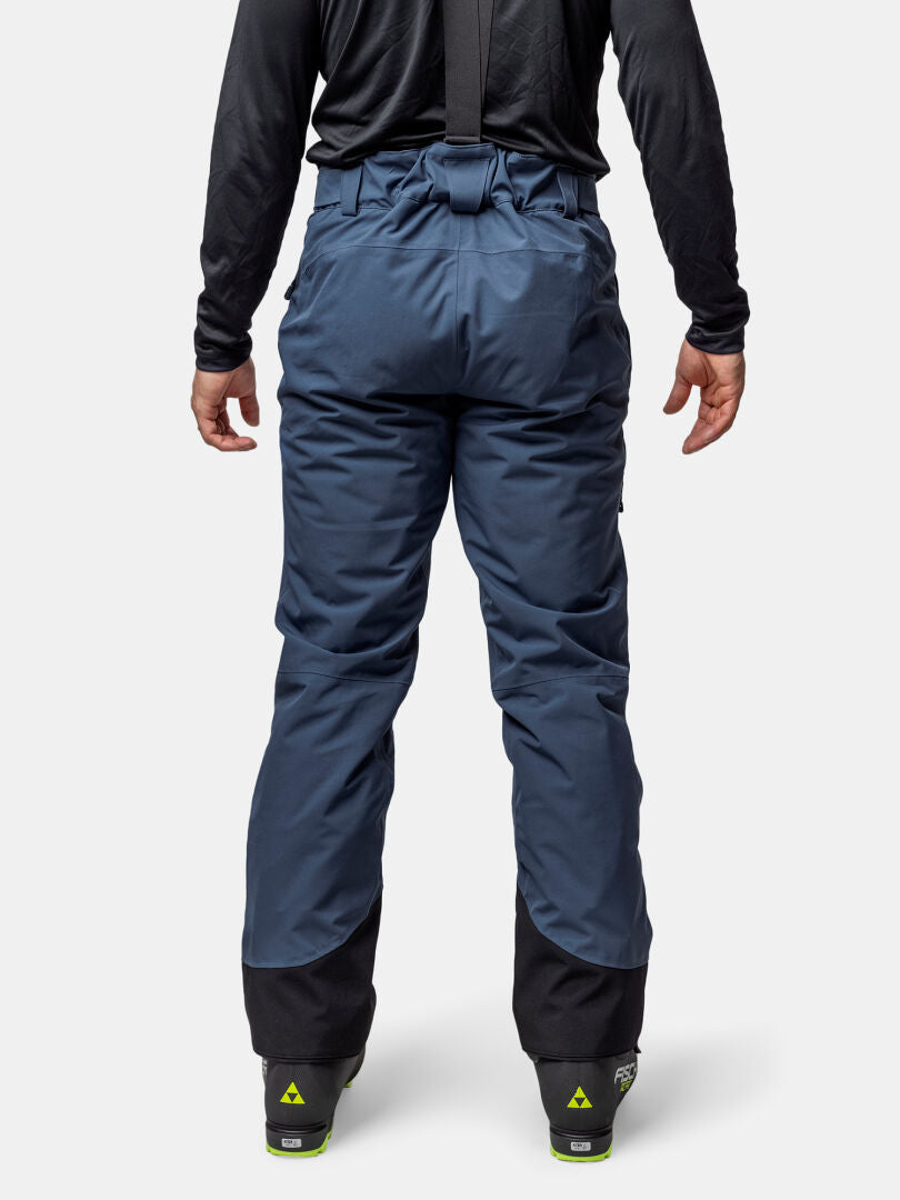 Person in blauer Halti Carvey II DX Skihose Herren mit DrymaxX, schwarzem Oberteil und Skischuhen, von hinten gesehen.