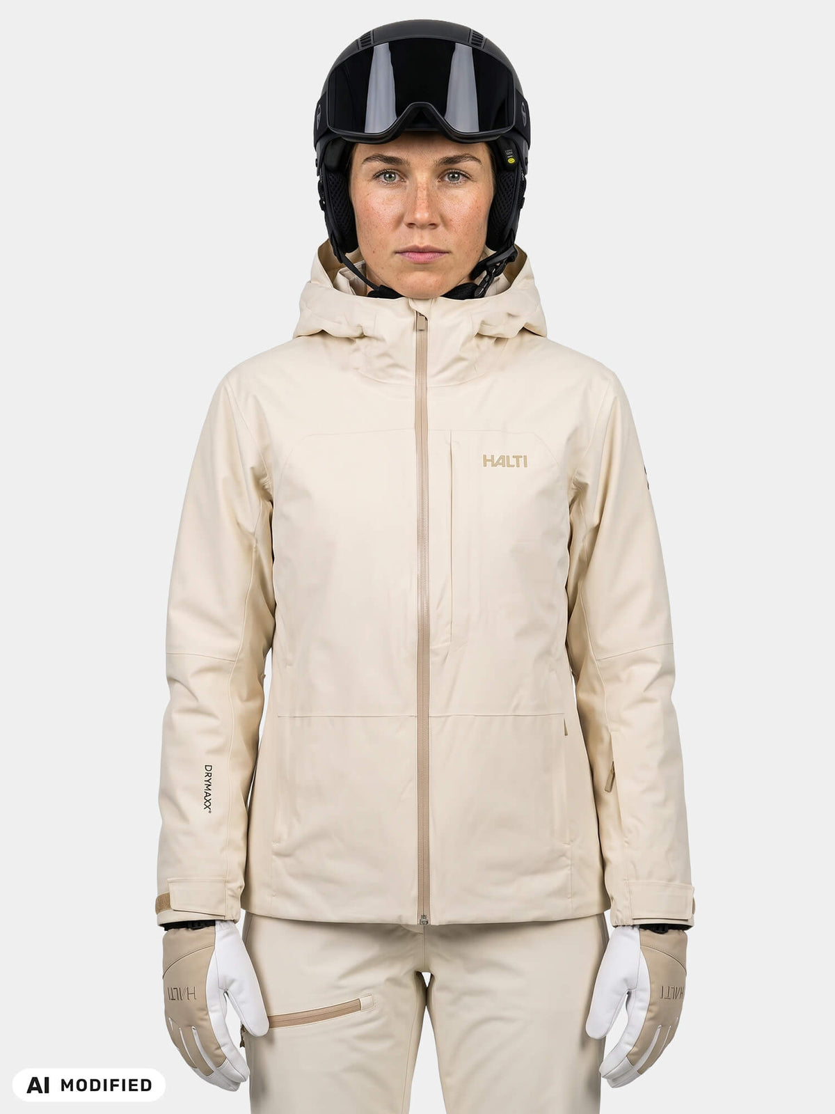 Eine Frau, die eine cremefarbene Halti Melvik DX Skijacke für Damen, einen Helm und eine Skibrille trägt.