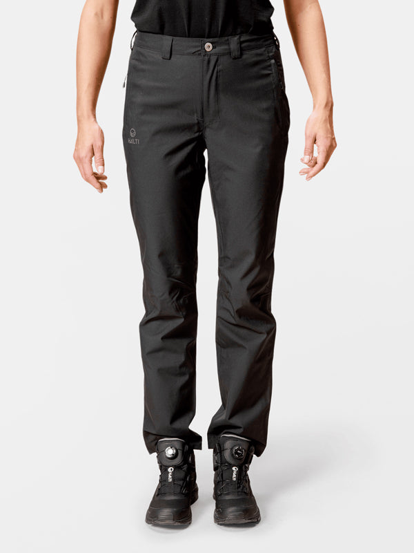 Frau in Halti Leisti DX Regenhose Damen und schwarzen Wanderschuhen steht entspannt vor einem weißen Hintergrund.