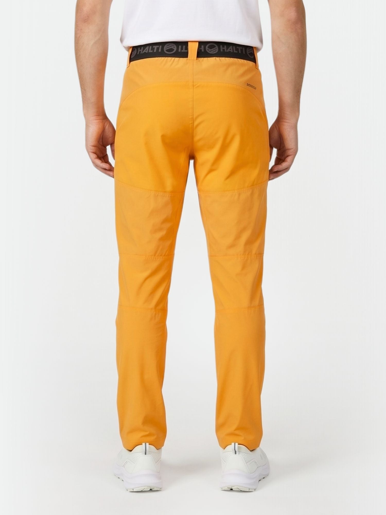 Eine Person in leuchtend orangefarbener Halti Pallas Herren X-stretch Lite Hose, weißem Hemd und Turnschuhen von hinten gesehen.