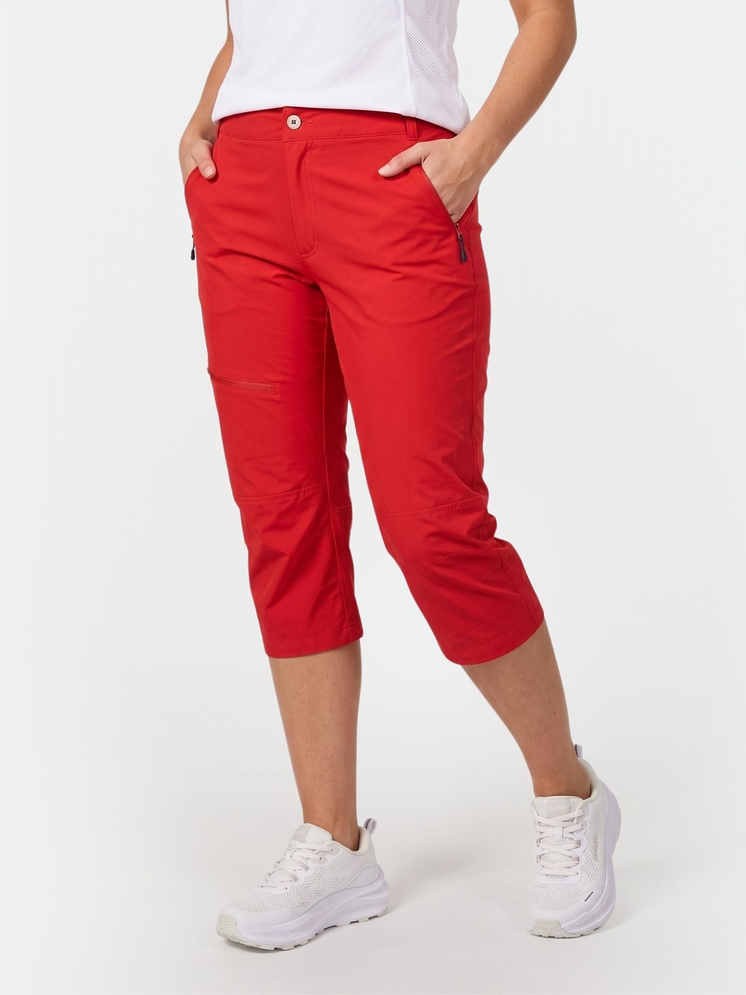 Model in Halti Pallas Damen X-stretch Lite Caprihose, weißen Turnschuhen und weißem Top steht mit den Händen in den Taschen.