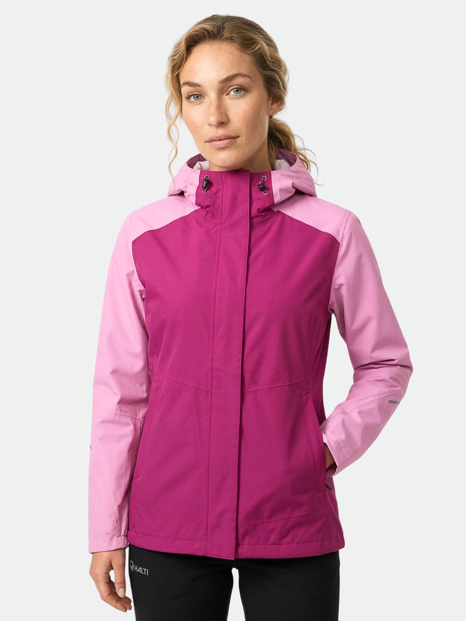Eine Frau trägt die Halti Fort DX Regenjacke Damen in zweifarbigem Rosa und steht mit einer Hand in der Tasche.