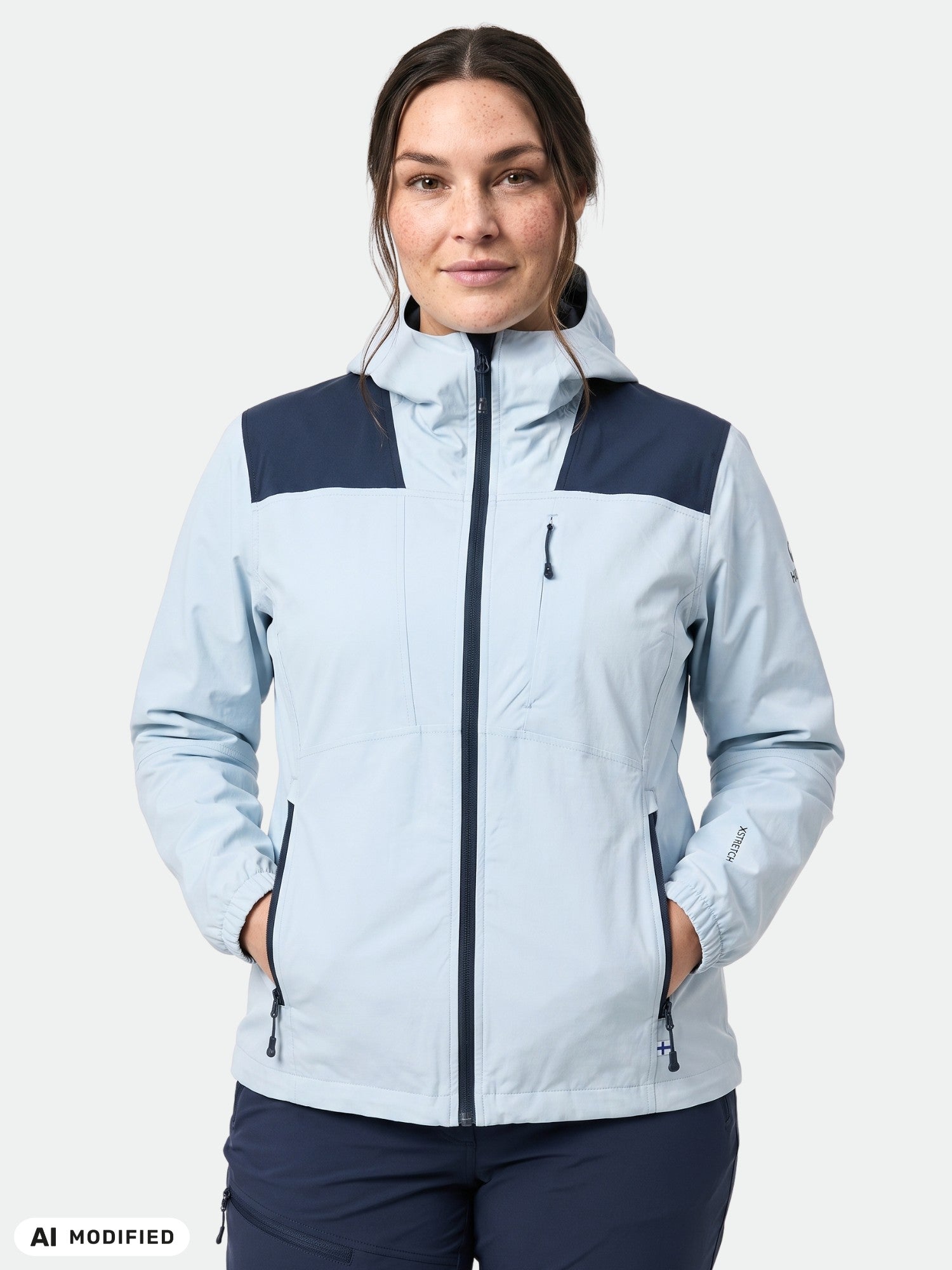 Frau in einer Halti Pallas II Plus Damen X-Stretch-Jacke, hellblau, Hände in den Taschen, einfarbiger Hintergrund.