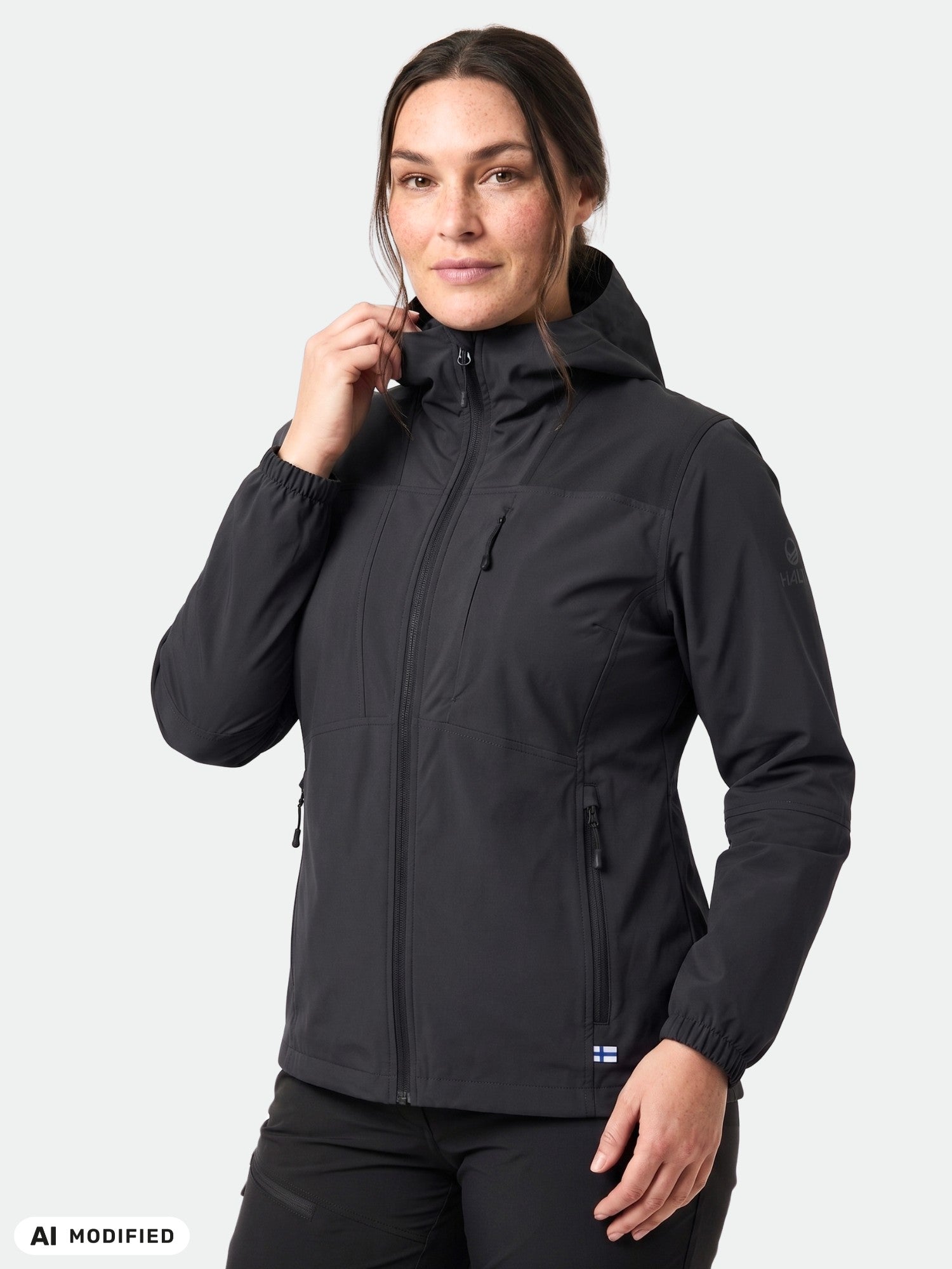 Eine Frau in einer schwarzen Halti Pallas II Plus Damen X-Stretch-Jacke blickt nach vorne und hält den Reißverschluss nahe an ihr Kinn.