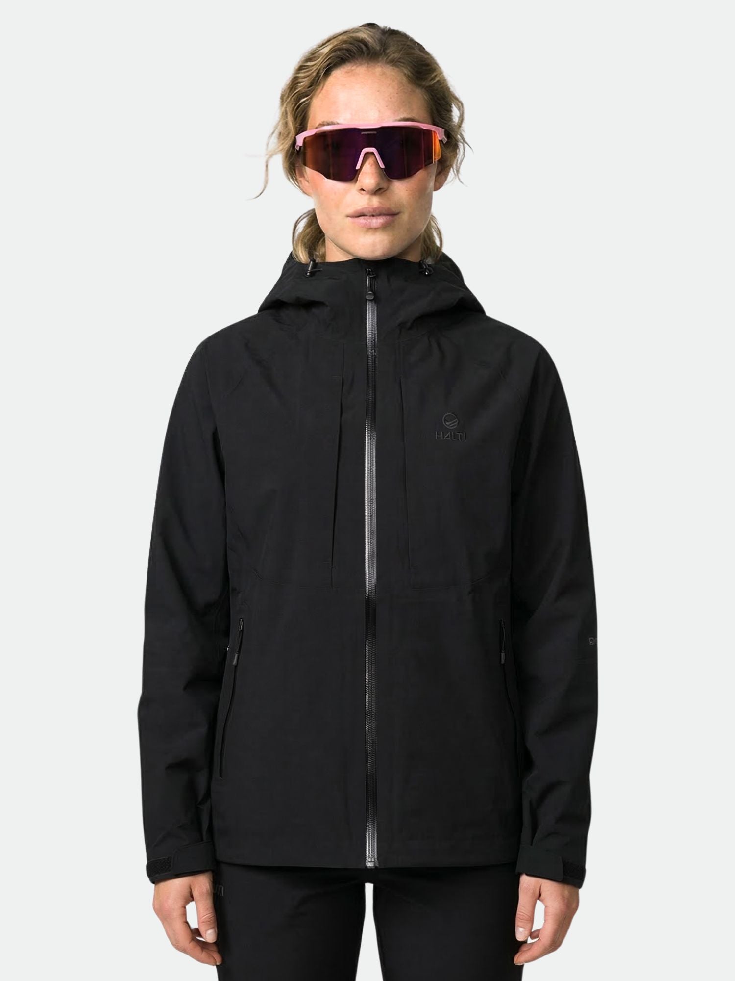 Eine Person in einer Halti Kaarna Damen DX 3L Regenjacke und einer reflektierenden Sonnenbrille steht vor einem schlichten Hintergrund.