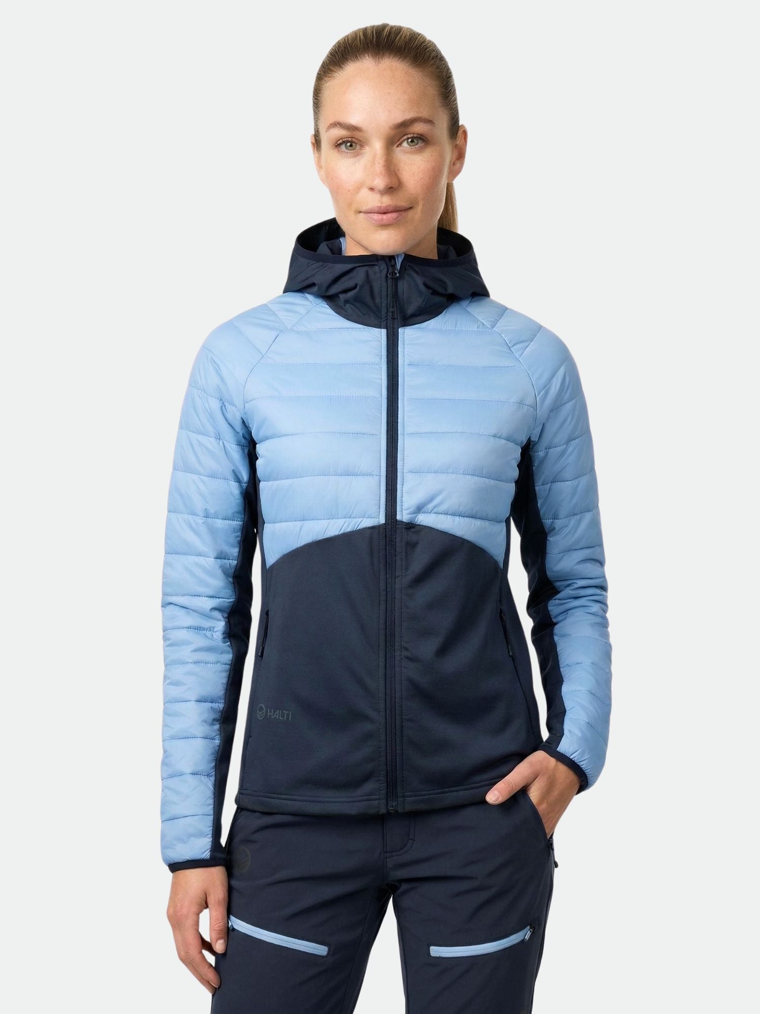 Eine Frau steht mit dem Gesicht nach vorne und trägt eine Halti Veidnes Damen Midlayer Jacke und eine passende marinefarbene Hose.