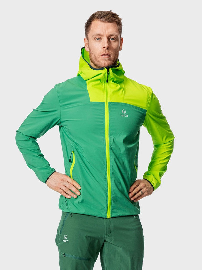 Ein Mann in einer grünen und gelben Halti Pallas Herren Lite X-stretch Jacke steht mit den Händen in den Hüften.