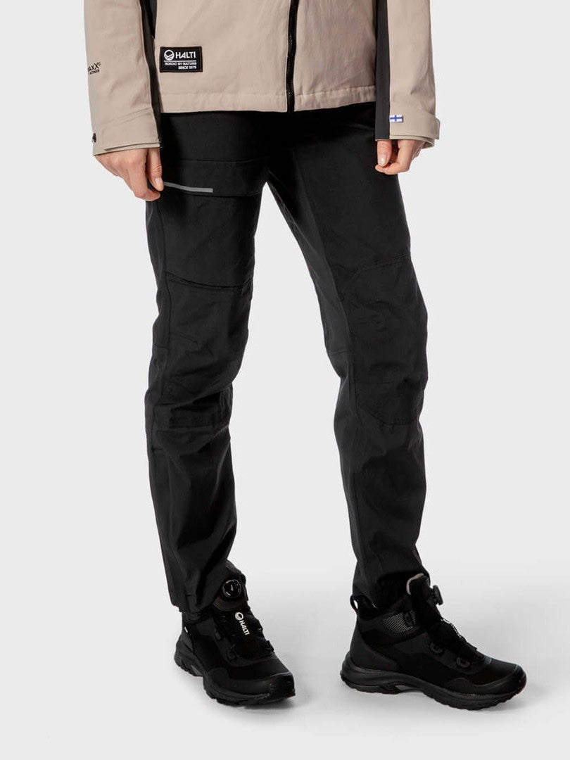 Person vor neutralem Hintergrund mit Halti Hiker Damen DrymaxX Hose, beige Jacke und schwarzen Wanderschuhen.