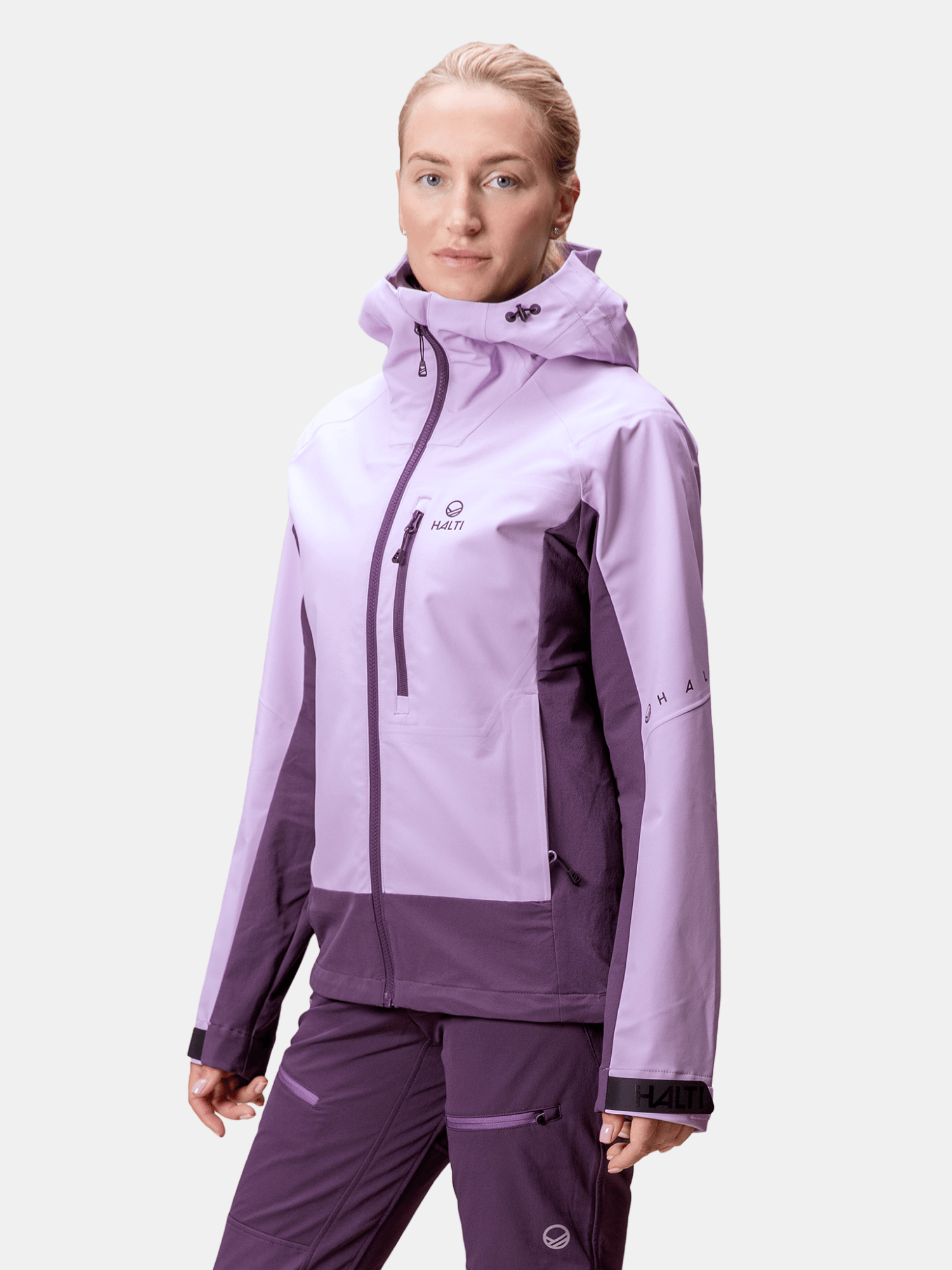 Eine Person trägt eine hellviolette Halti Pallas III Damen Warm Hybrid Jacke und eine dazu passende Hose vor einem schlichten Hintergrund.