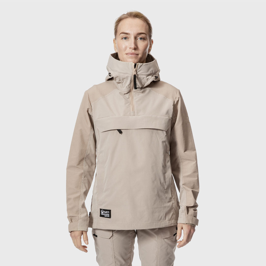 Eine Person steht mit Blick nach vorne in einem beigen Halti Hiker Damen Lite Anorak aus recyceltem Nylon vor einem weißen Hintergrund.