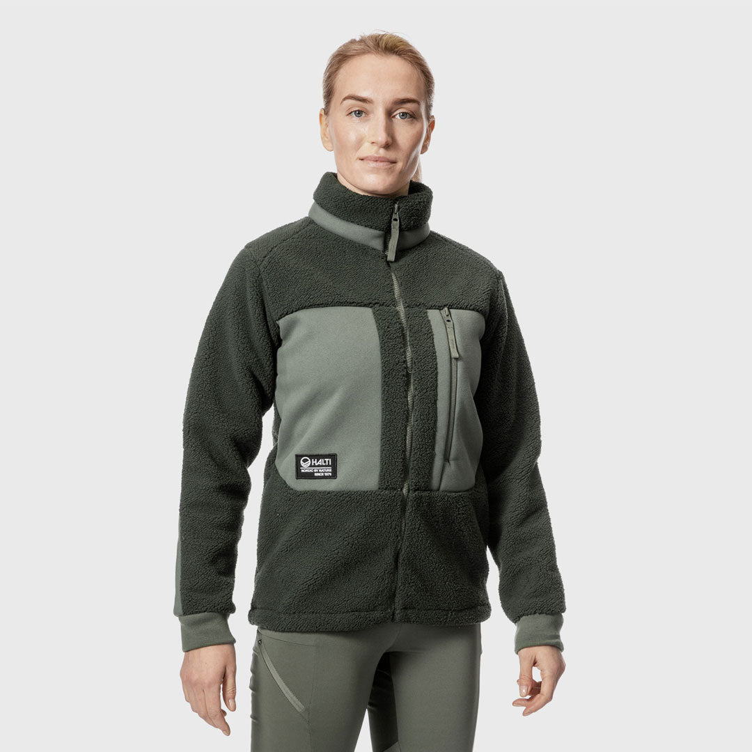 Eine Person, die eine zweifarbige grüne Fleecejacke und eine dazu passende Hose trägt, steht mit dem Gesicht nach vorne vor einem schlichten hellen Hintergrund.