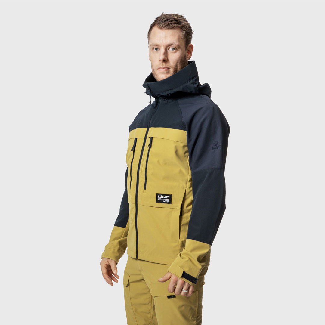 Ein Mann trägt eine gelb-schwarze Halti Hiker Herren Lite Outdoor-Jacke und eine passende Hose vor einem hellgrauen Hintergrund.