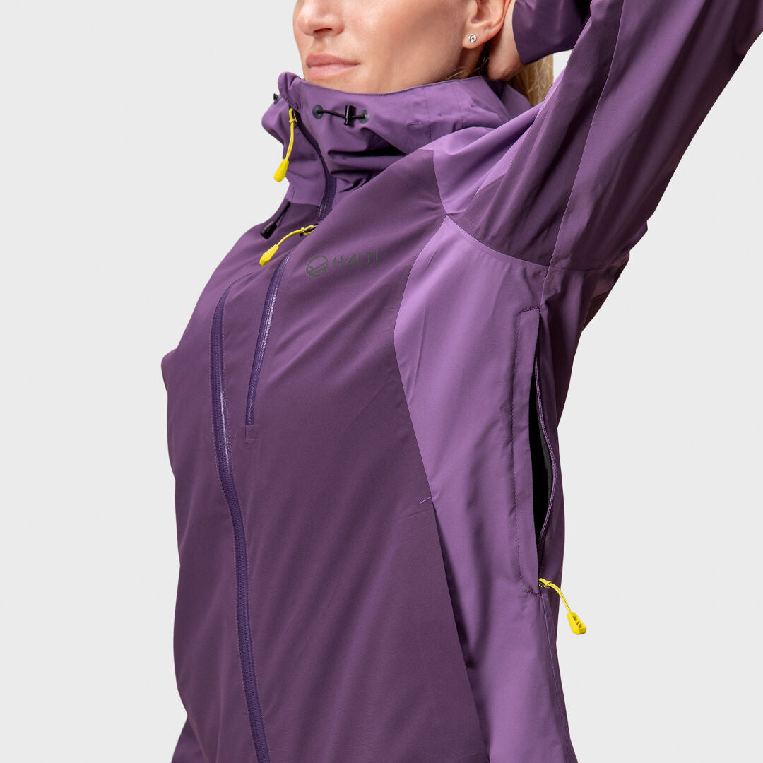 Eine Frau in einer lilafarbenen Halti Biegga Neve DrymaxX Regenjacke hebt einen Arm und gibt den Blick auf den seitlichen Reißverschluss und den hohen Kragen frei.