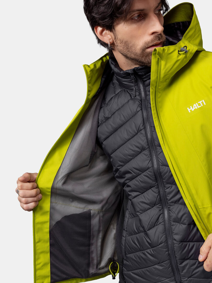 Ein Mann öffnet seine leuchtend gelbe Halti Forter DX Regenjacke Herren, um eine schwarze, gesteppte Innenjacke mit Netzfutter zum Vorschein zu bringen.