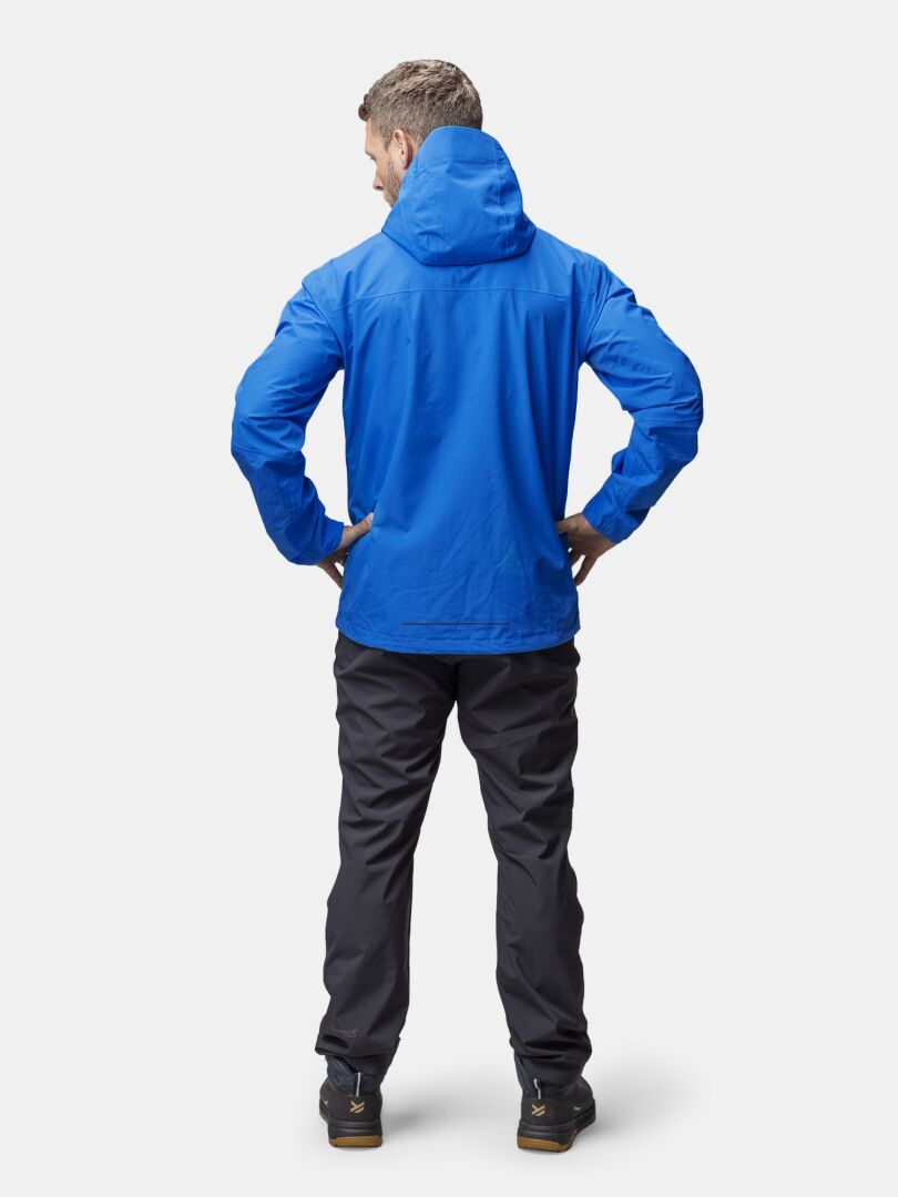 Ein Mann steht in einer blauen Halti Forter DX Regenjacke Herren und einer schwarzen Hose, bereit für Aktivitäten im Freien.