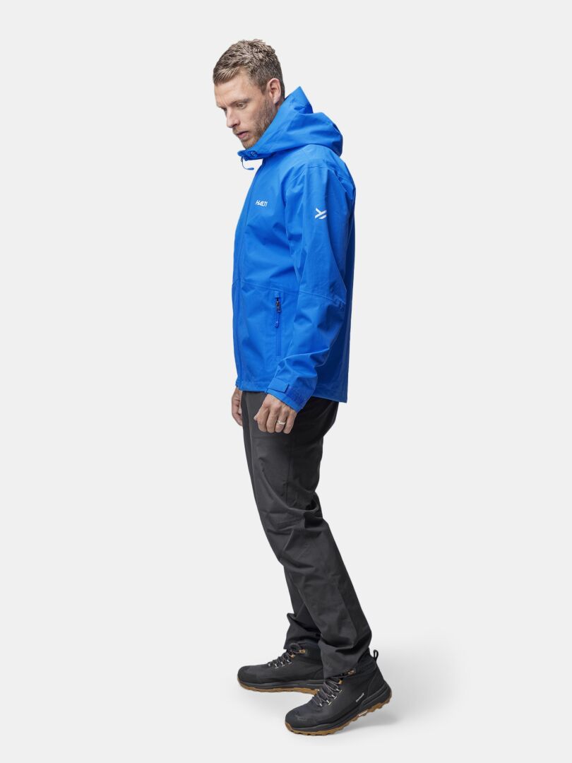 Ein Mann trägt die Halti Forter DX Regenjacke Herren, dunkle Hosen und Wanderschuhe vor weißem Hintergrund.