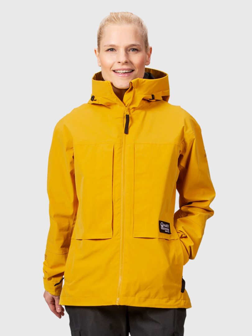 Eine Frau in einer gelben Halti Hiker II DrymaxX Regenjacke steht mit Blick nach vorne – ideal für Outdoor-Enthusiasten.
