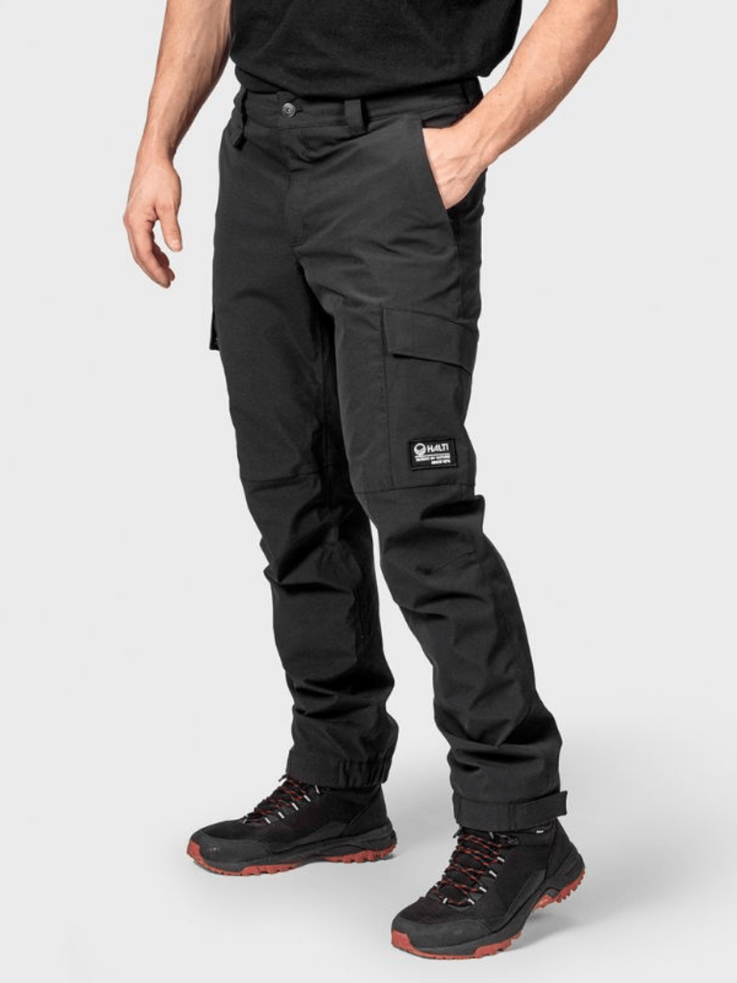 Eine Person in Halti Hiker II DrymaxX Hosen Herren und schwarzen Stiefeln steht vor einem schlichten Hintergrund.