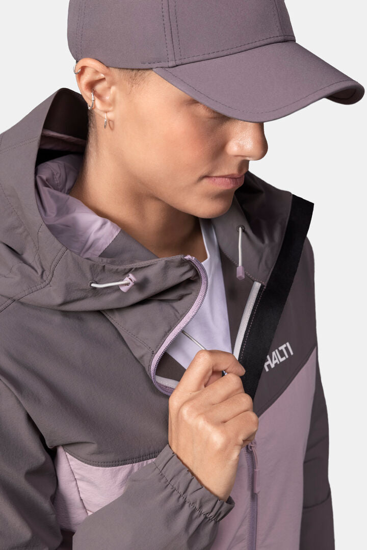 Eine Frau in einer Halti Pallas Evo X-Stretch-Jacke und Mütze zieht den Reißverschluss ihrer Jacke hoch und schaut nach unten.